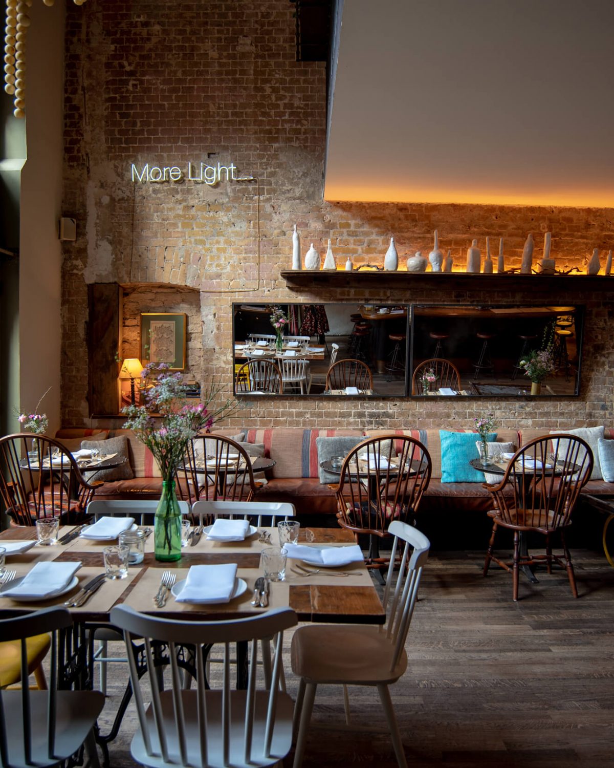 Stylishly furnished room on the ground floor of a Berlin restaurant with rustic brick walls, neon 'More Light' lettering, set tables and cosy seating areas.