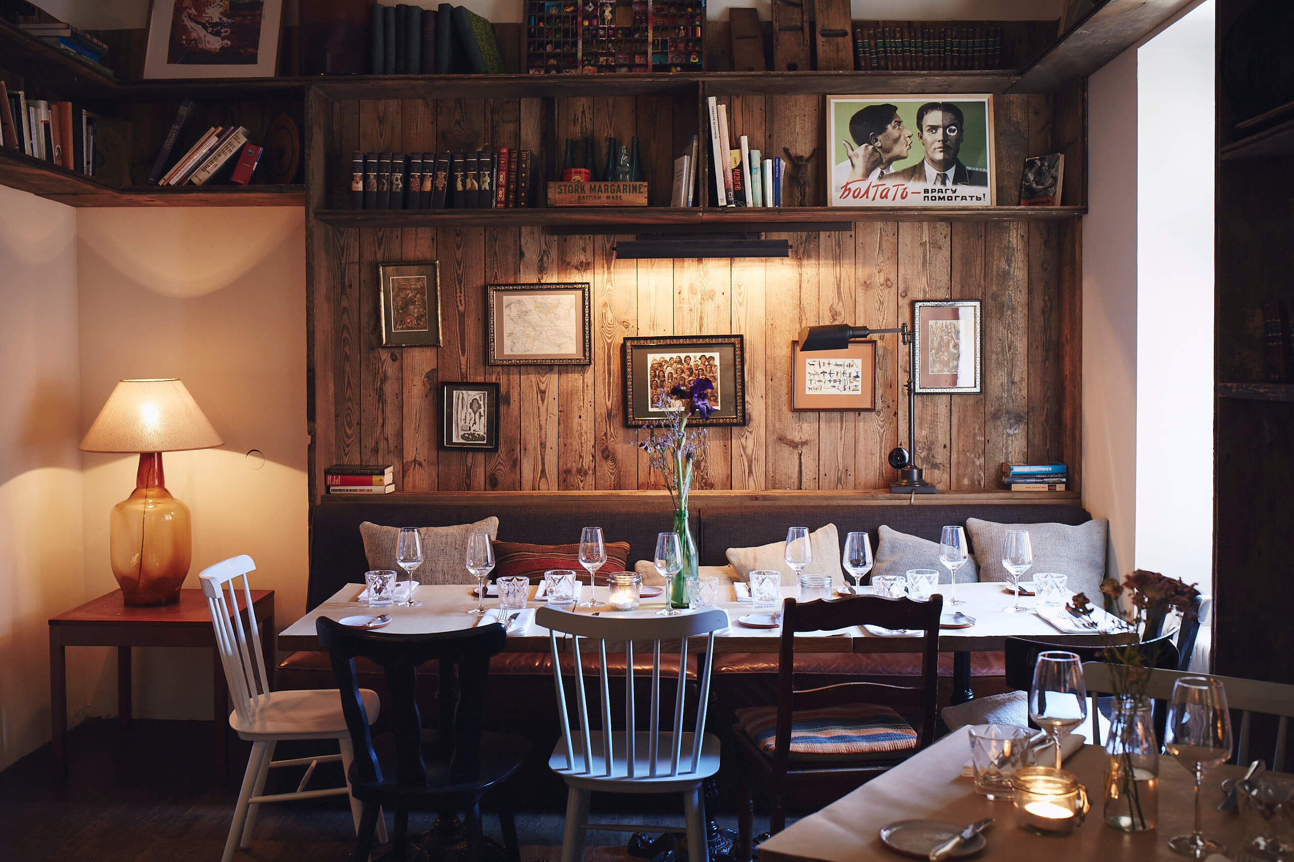 Intimately furnished room 'The Library' with bookshelves, wooden walls, eclectic artwork and set tables, ready for 40 guests.
