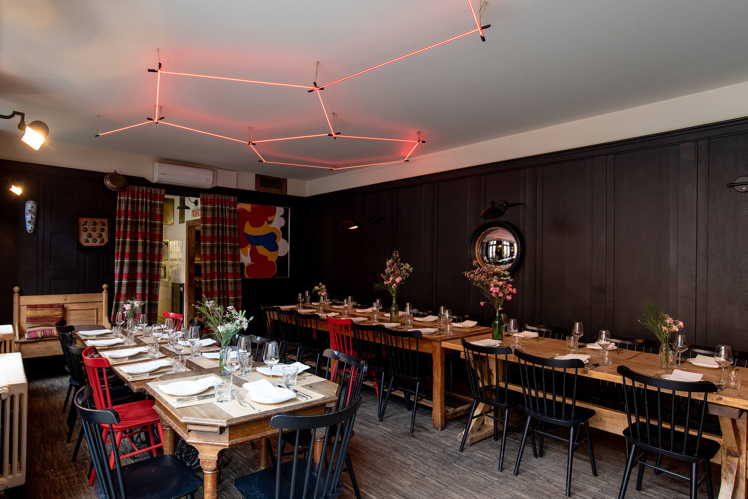 Stylishly furnished panel room with long wooden table, set for 35 guests, red neon light on the ceiling and artistic mural.